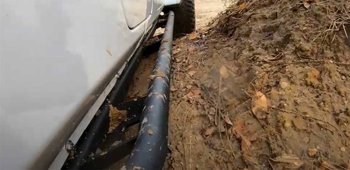 Black tubular nerf bar mounted along the side of a white truck bed next to muddy, dirt-covered ground