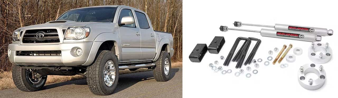 Suspension lift kit components laid out including two silver shock absorbers, spacers, brackets, bolts, and hardware for