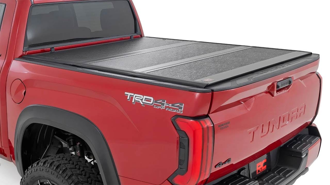 Red pickup truck bed with dark gray tonneau cover featuring horizontal panels, partially open