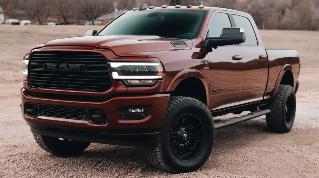 Burgundy Ram pickup truck with black grille and roof rails parked on dirt ground