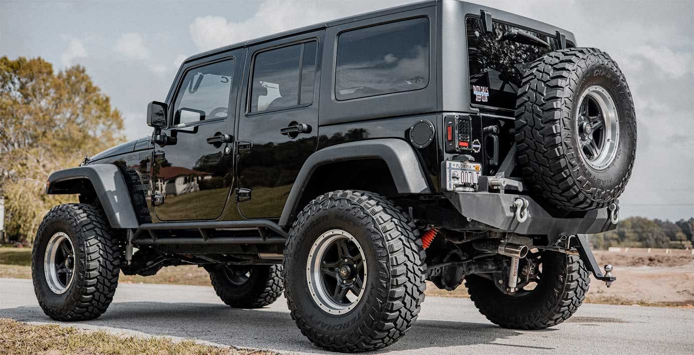 Black lifted Jeep Wrangler with oversized all-terrain tires, rear tire carrier, and lifted suspension on paved ground