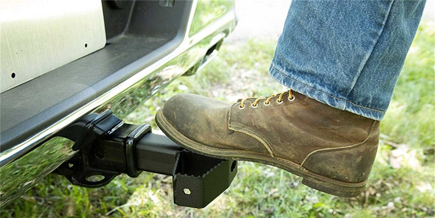 Boot stepping on a black truck step attached below the door, with grass visible in background