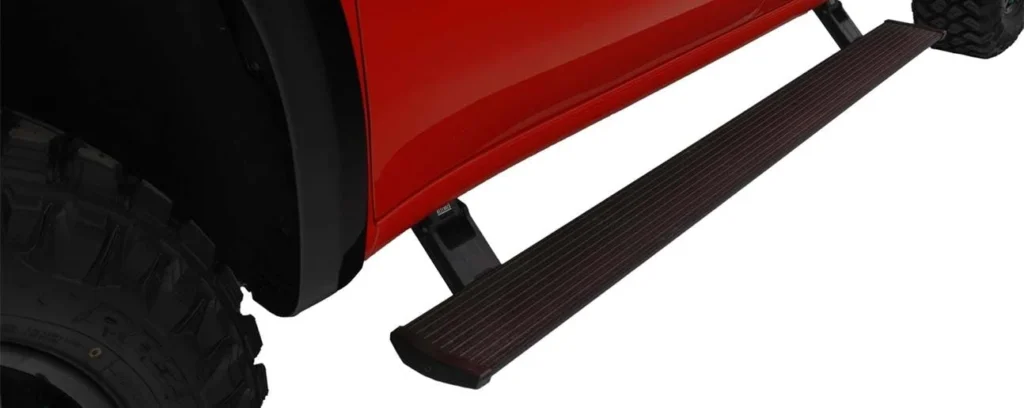 Black running board mounted beneath the door of a red truck, with textured surface and metal brackets