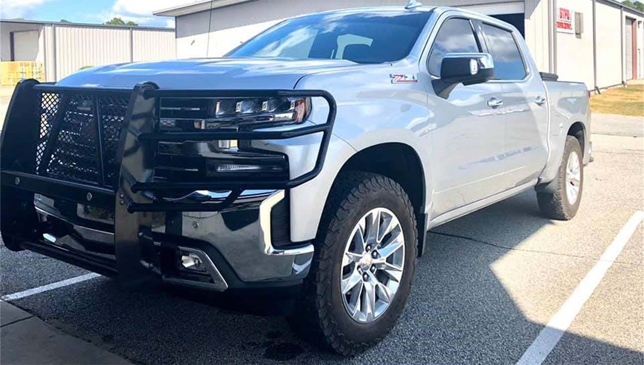 Silver pickup truck with black steel grille guard protecting the front bumper and headlights in a parking lot