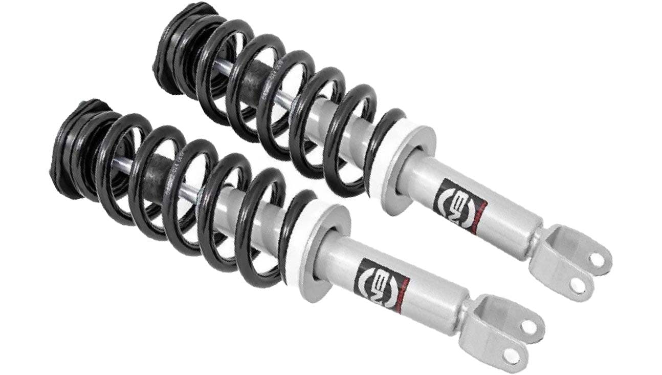 Pair of coilover suspension struts with white cylinders and black coil springs mounted on mounting brackets.