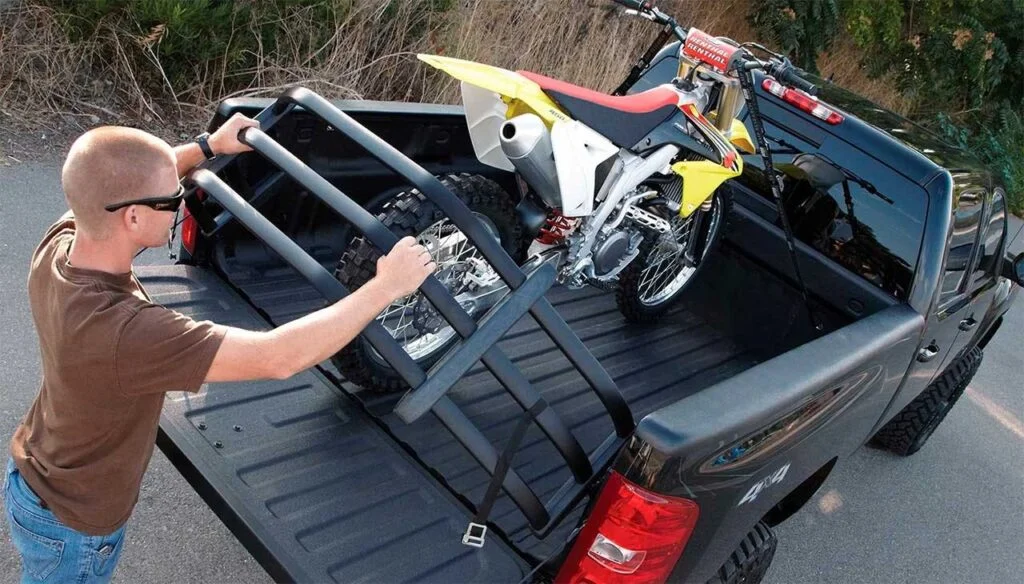 Man securing a yellow dirt bike to a black truck bed extender frame mounted on the tailgate