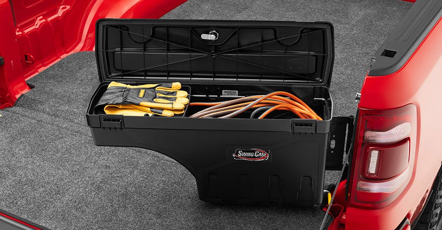 Black toolbox open in red truck bed, displaying hand tools and orange extension cord inside.