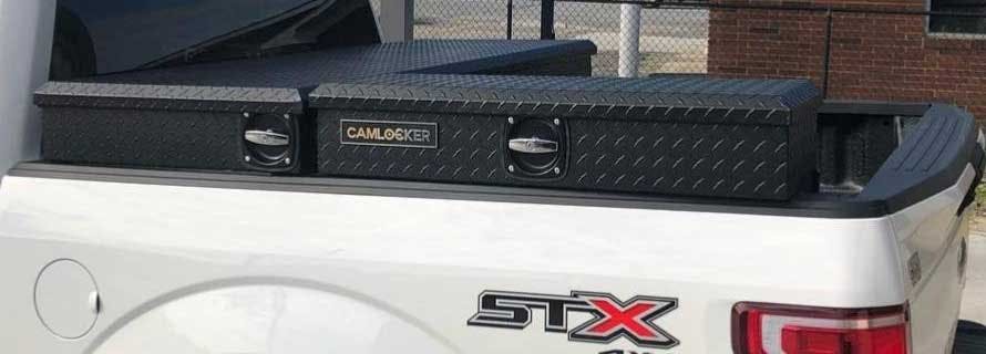Black diamond-plate Camlocker toolbox mounted across the back of a white pickup truck bed.