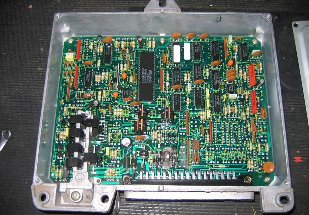 Computer circuit board with green background, black components, orange capacitors, and white connector pins in clear plastic
