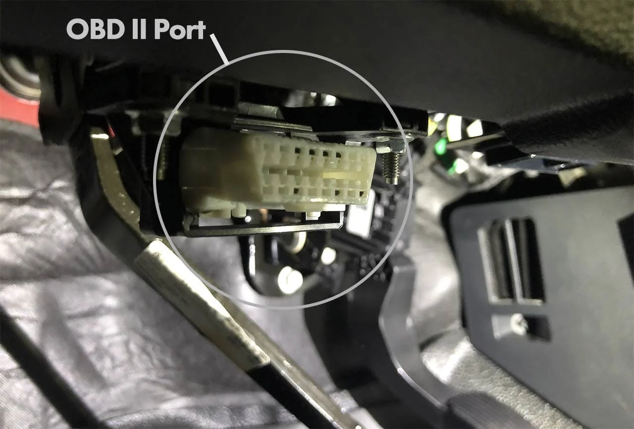 Beige OBD II port connector highlighted with circle on vehicle dashboard interior