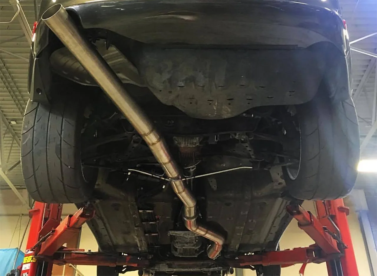 Underside of truck showing polished metal exhaust pipes and muffler mounted on red support frame in garage