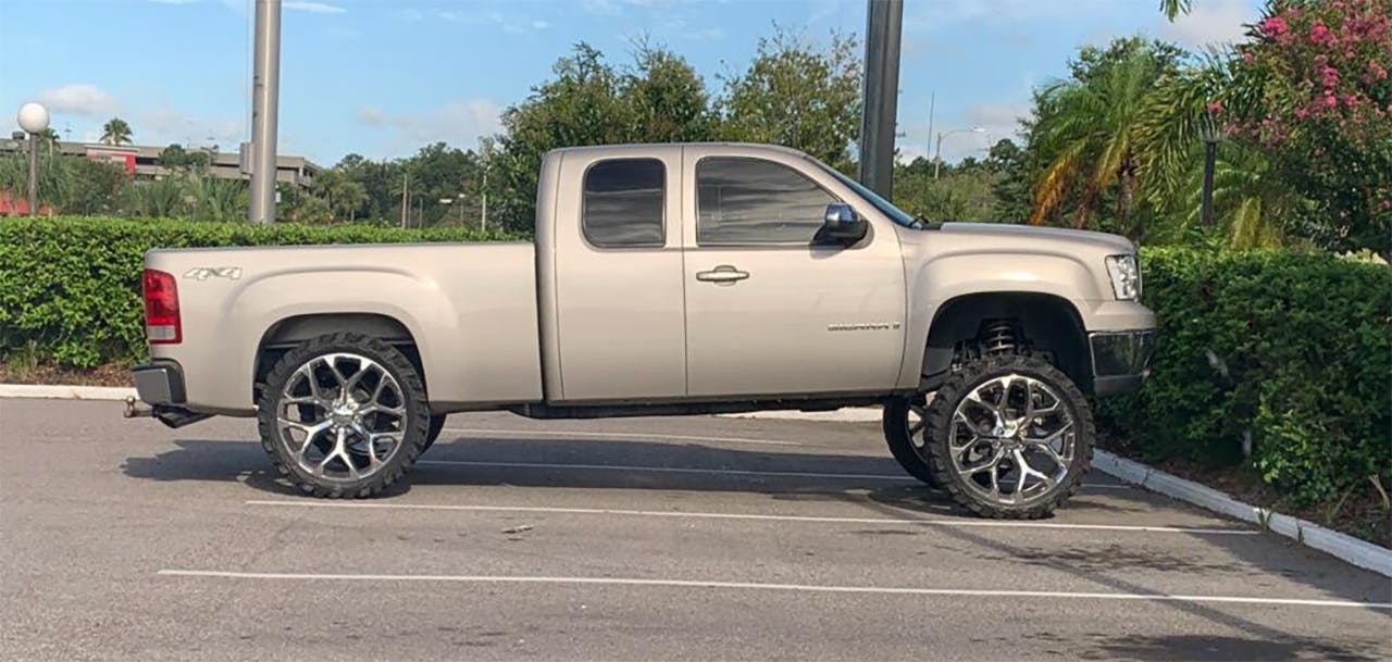 Lifted silver pickup truck with oversized chrome wheels parked in a lot, front end jacked up much higher than the rear.