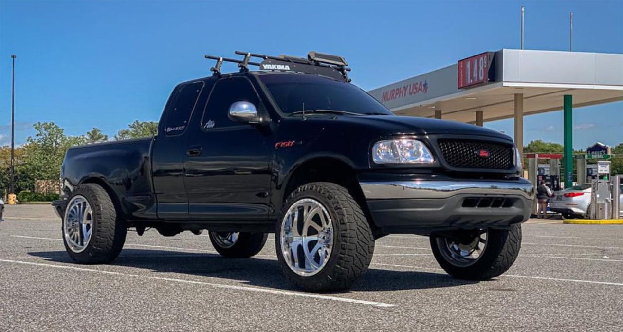 Black pickup truck with chrome wheels and roof rack at a gas station, front suspension lifted higher than the rear in a