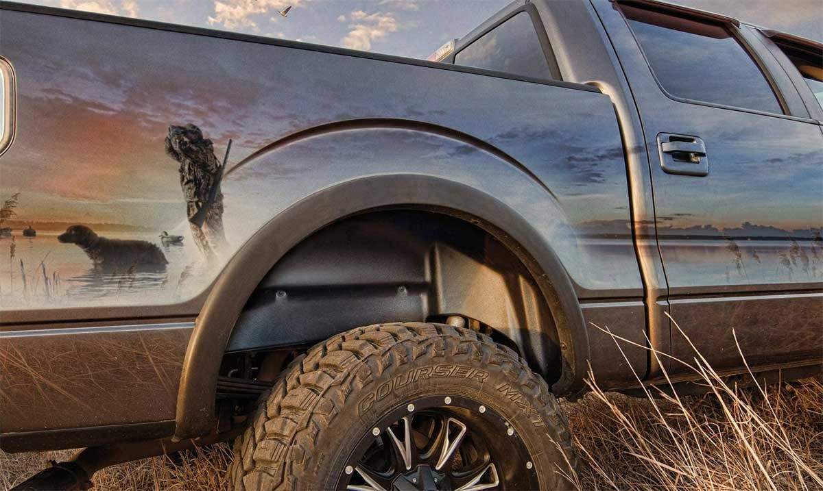 Truck wheel well showing a rugged terrain tire with metal rim and black fender liner installed inside the wheel opening.