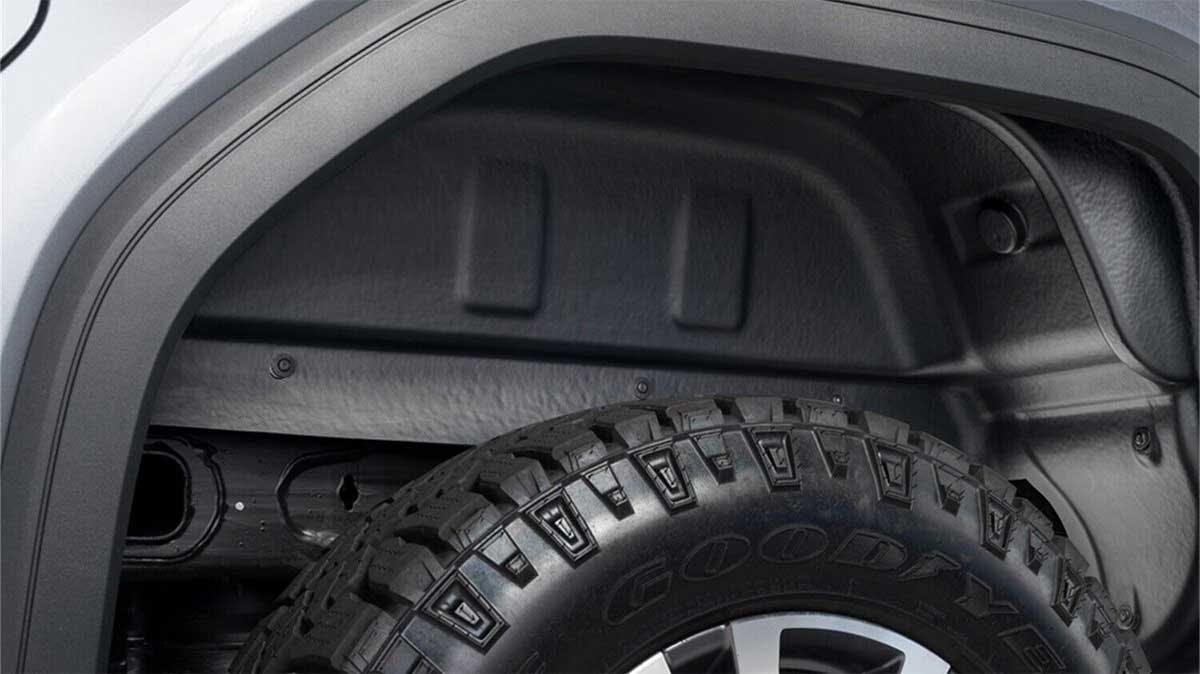 Black powder-coated steel inner fender liner installed inside a truck's wheel well above an off-road tire