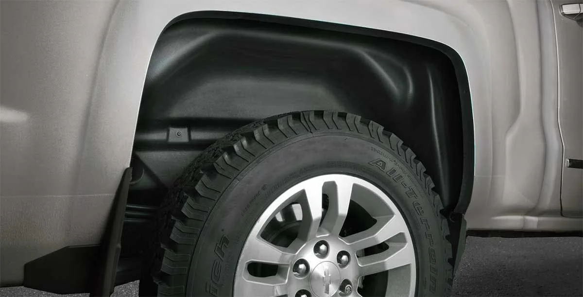 Black plastic wheel well liner installed above a silver alloy wheel with all-terrain tire on truck fender