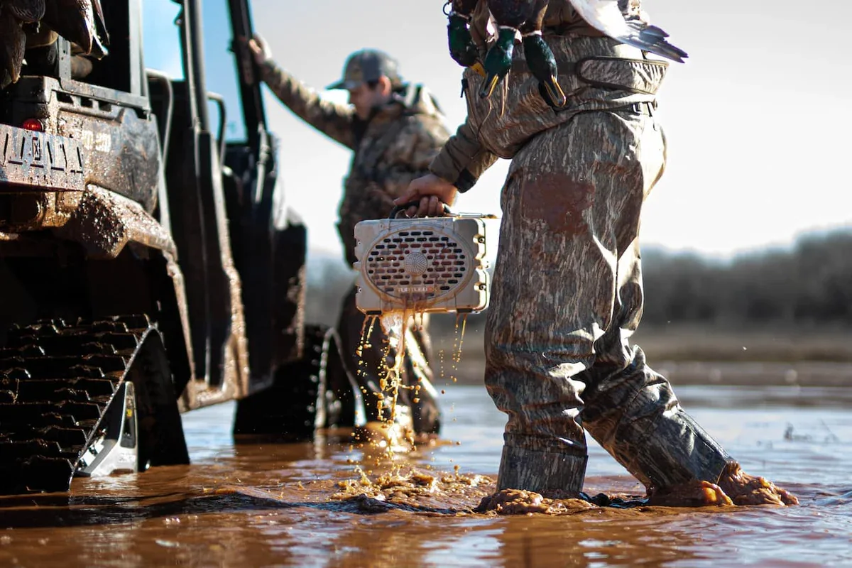 A Turtlebox speaker being lifted dripping out of flooded timber on a duck hunt